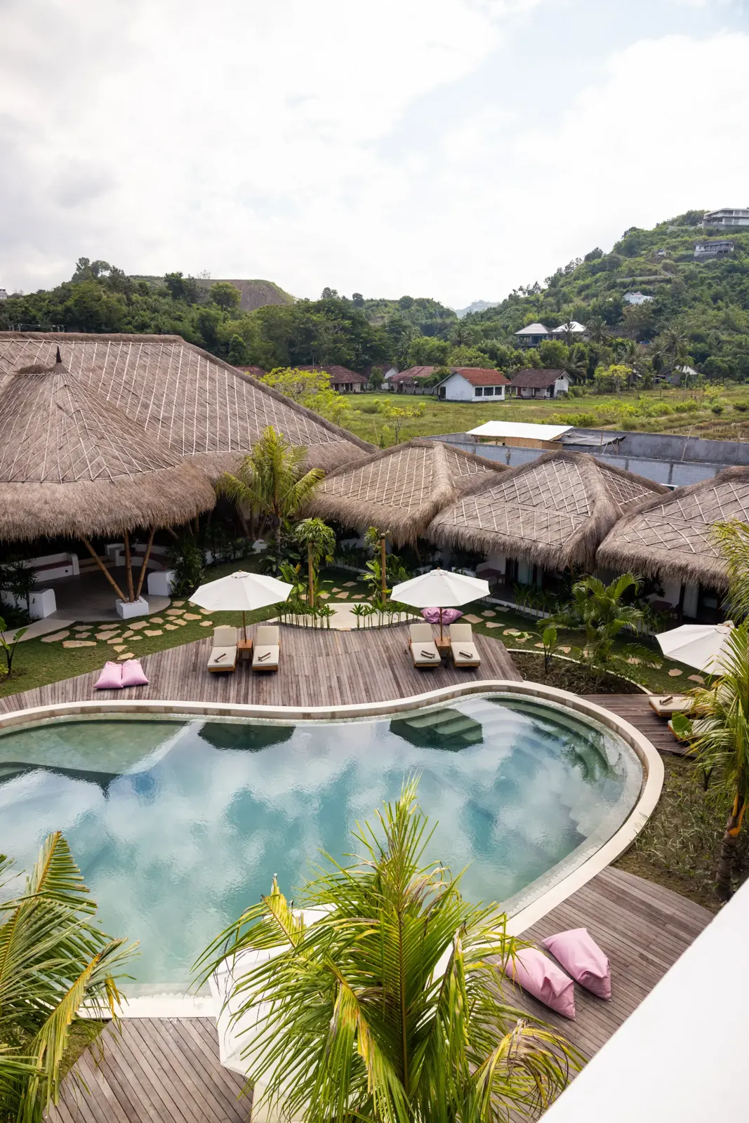 Aerial view of the pool and thatched roofs with hills in the distance