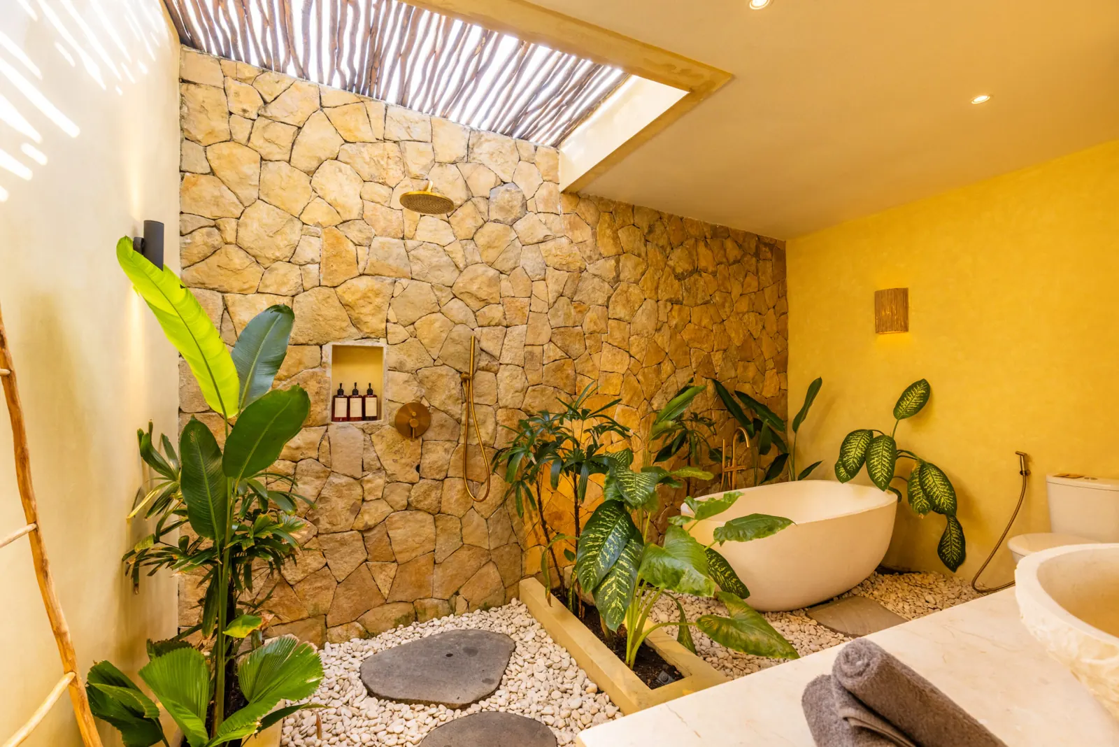 Stone-walled bathroom with skylight, bathtub and tropical plants