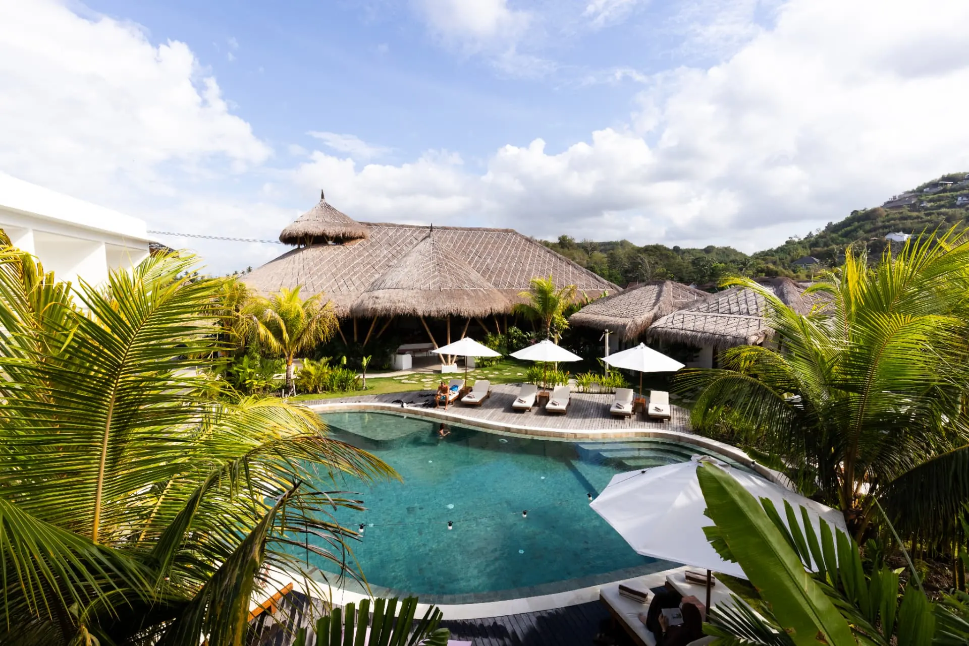 Pool and thatched pavilions among palms at Uryah Hotel Lombok, with green hills behind