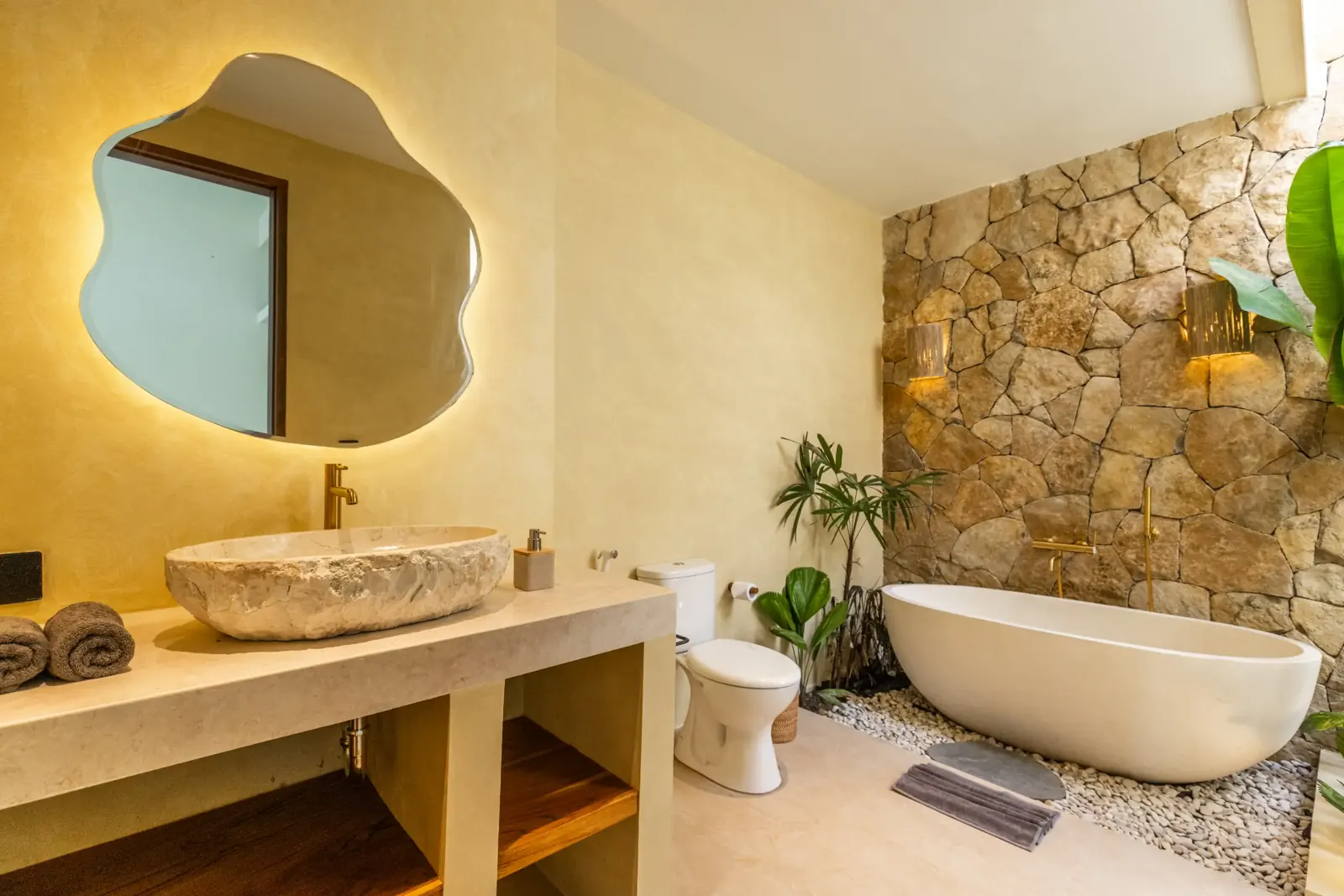 Bungalow bathroom with stone vanity, freestanding bathtub and stone wall