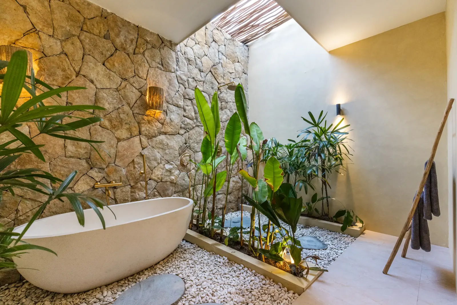 Open-air bungalow bathroom with freestanding bathtub and tropical plants